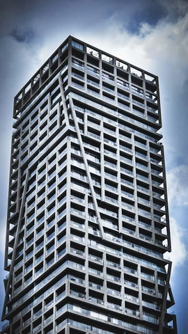 Grand bâtiment moderne avec structure extérieure anguleuse et fenêtres rectangulaires sous un ciel nuageux