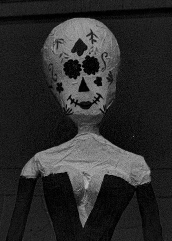 Paper-mâché skull and torso figure wearing a v-neck suit