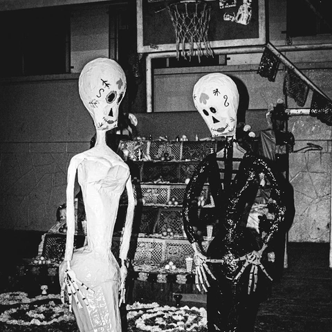 deux figures squelettiques en papier mâché devant une offrande avec un ballon de basket en arrière-plan