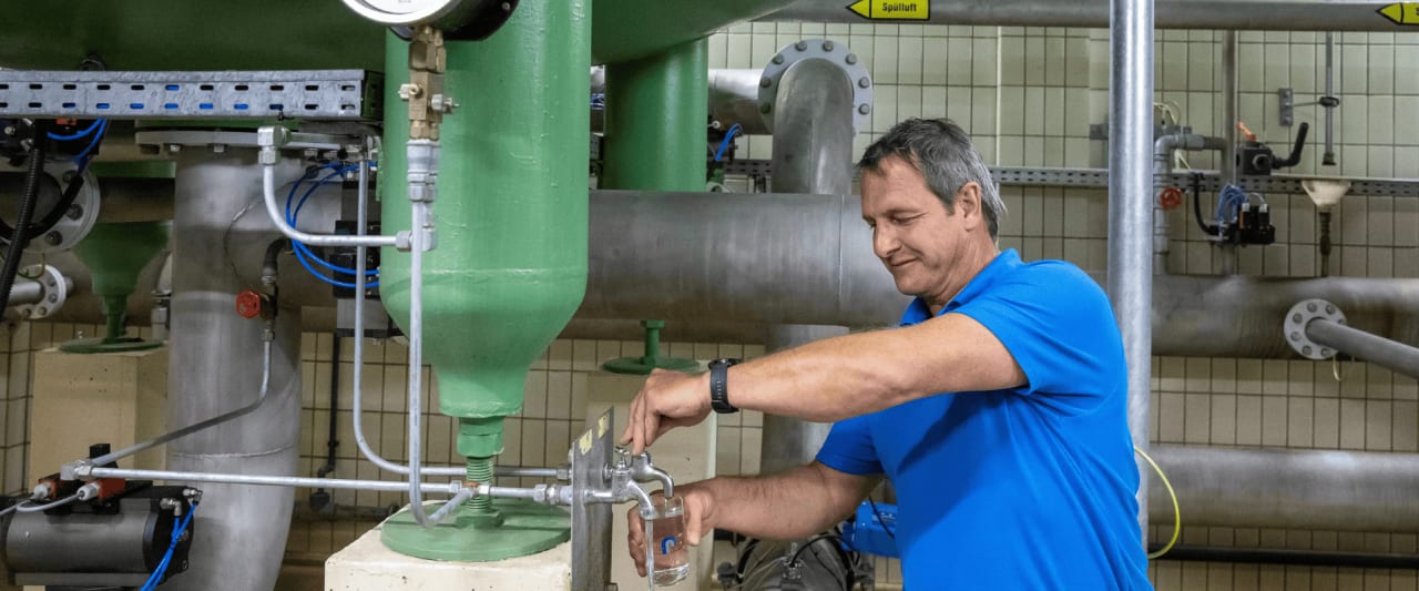 Mann zapft in einer technischen Anlage Wasser aus dem Hahn.