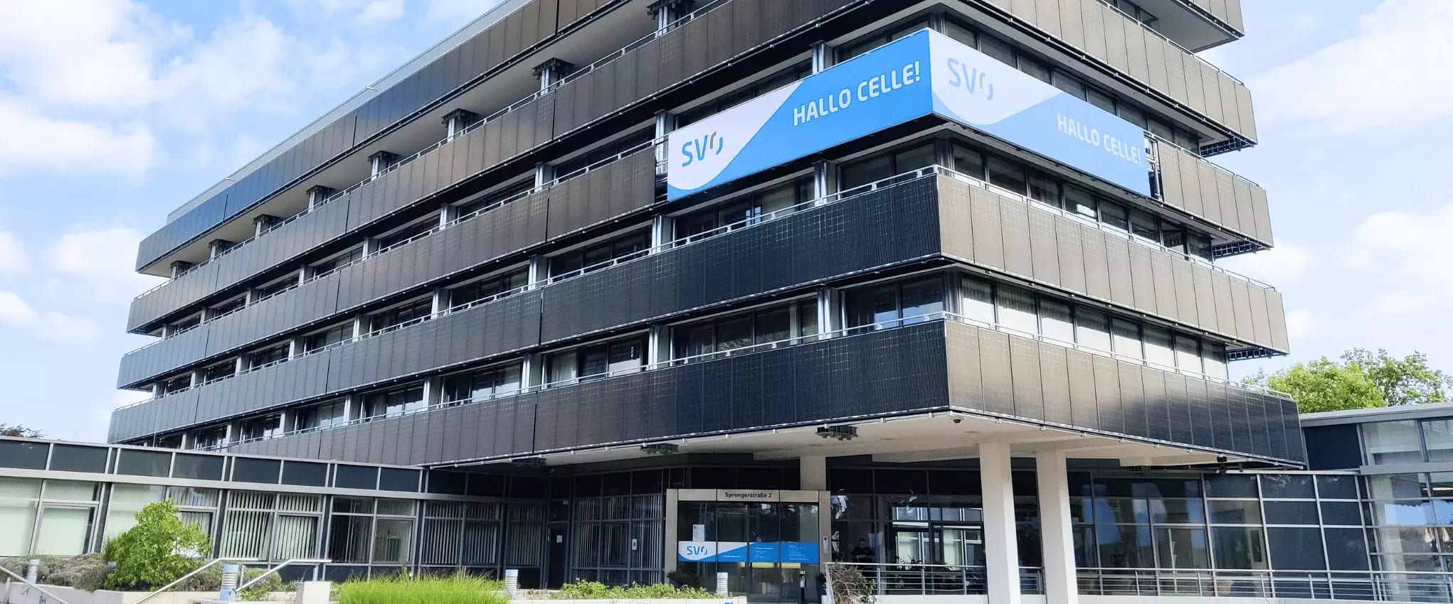 Außenansicht eines modernen Bürogebäudes der SVO mit LED-Werbetafel und der Aufschrift „Hallo Celle!“.