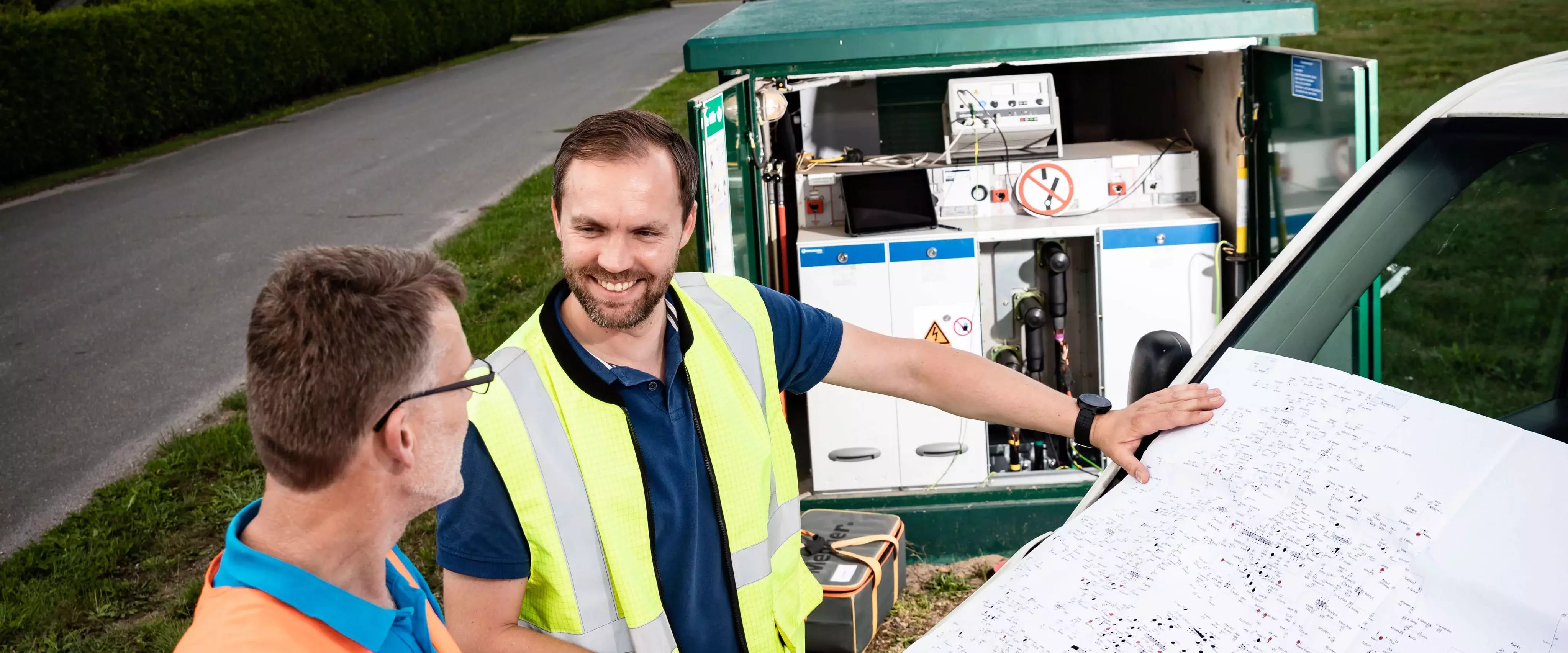 Arbeiter betrachten Plan vor offener Trafostation