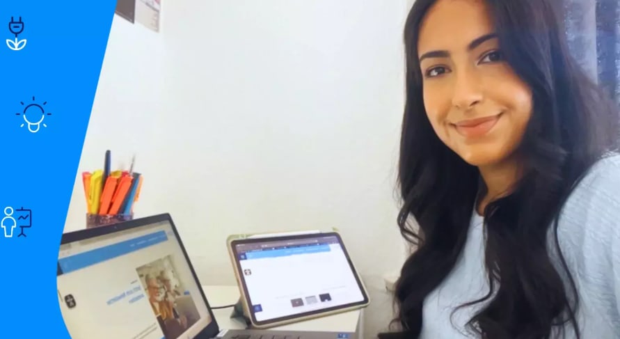 Junge Frau arbeitet an Laptop und Tablet im Homeoffice und lächelt in die Kamera.