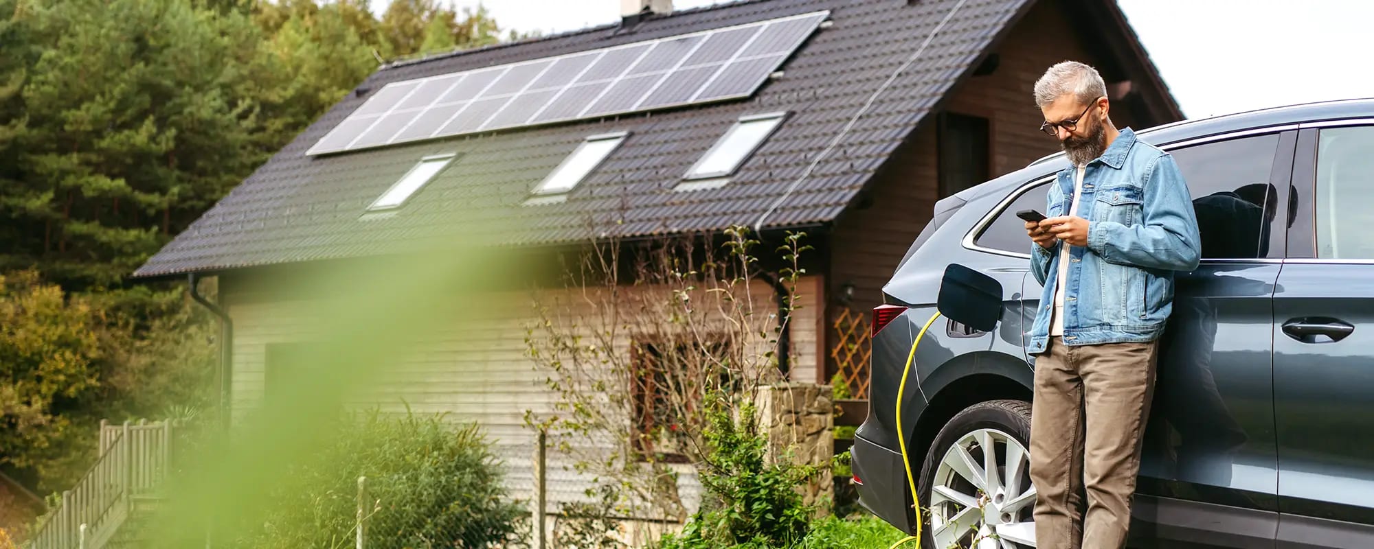 Mann lädt E-Auto vor Haus mit Photovoltaik