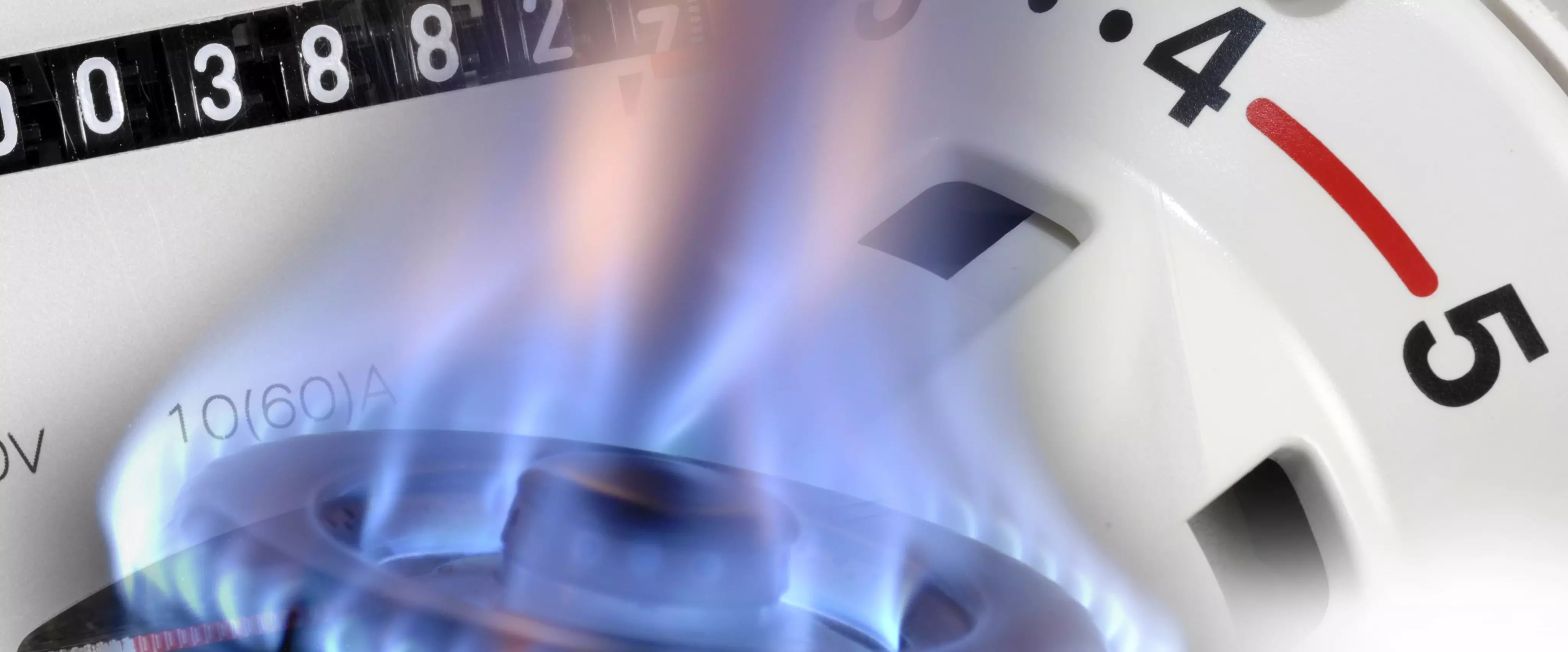 Flamme eines Gasherdes mit Thermostat und Gaszähler im Hintergrund