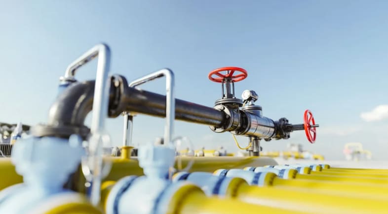 Detailaufnahme eines Gas- oder Ölpipelinesystems im Freien mit mehreren gelben Rohren, blauen Ventilen und roten Handrädern unter blauem Himmel.