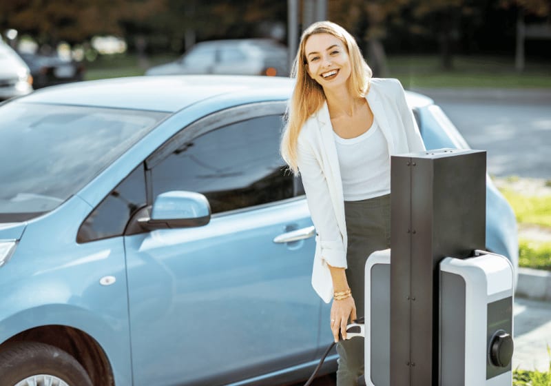 Junge Frau lädt ein Elektroauto an einer Ladesäule.