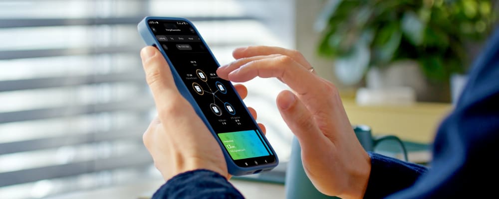 Person bedient Smartphone mit Energiemanagementsystem zur Steuerung des Energieverbrauchs und der Geräte.