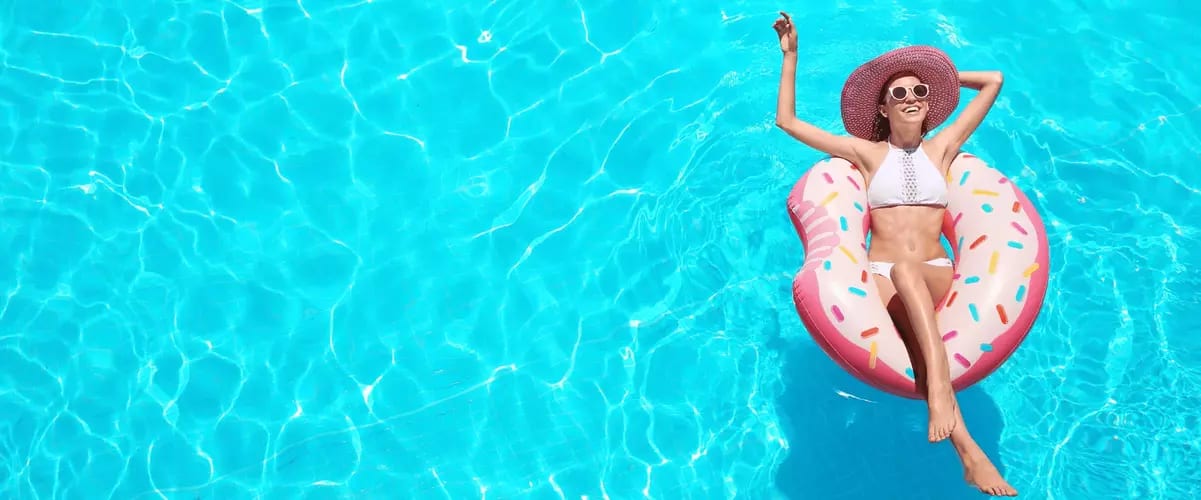 Frau in weißem Bikini und Sonnenhut entspannt auf einer Donut-förmigen Luftmatratze im klaren, türkisfarbenen Pool.