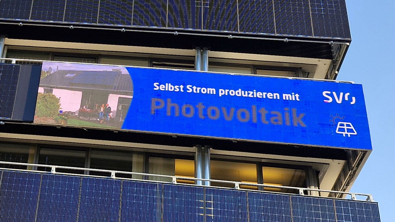 Eine digitale Werbetafel an einer Gebäudefassade wirbt für Photovoltaik-Technik.