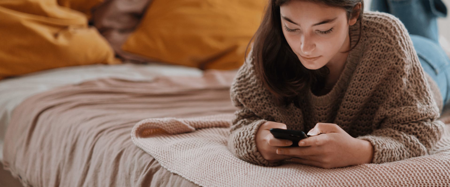 Junge Frau auf dem Bett mit einem Handy in der Hand.