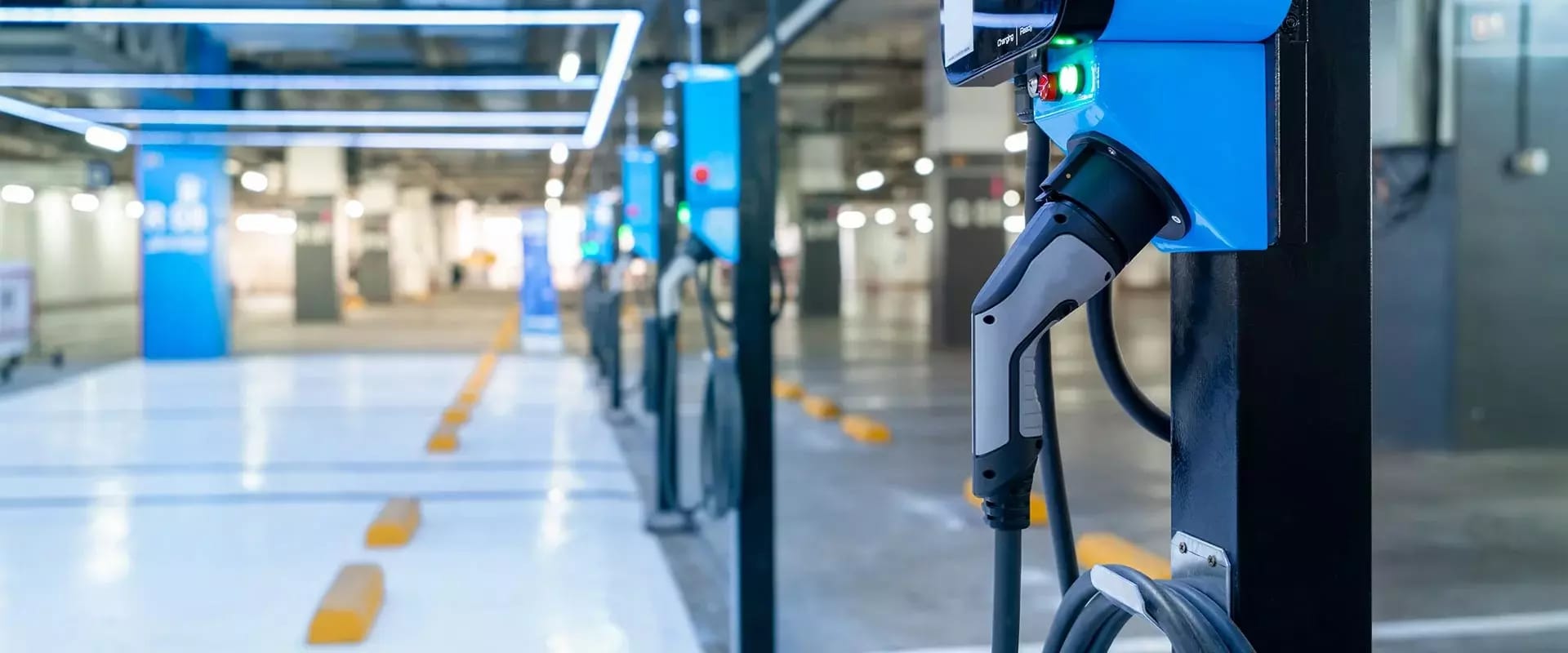 Mehrere blaue E-Ladesäulen mit Ladekabeln in einer hell beleuchteten Tiefgarage.