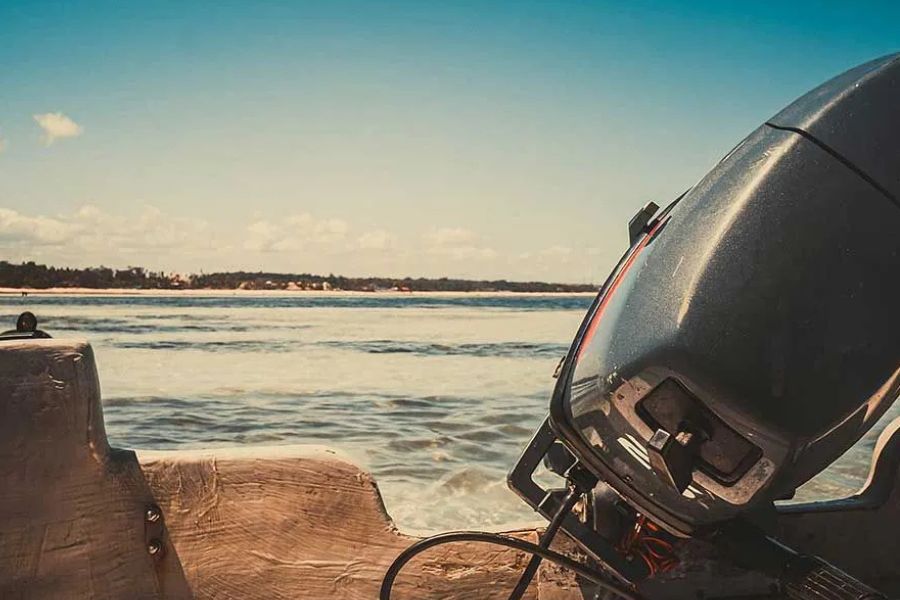 Close-up of a boat's outboard motor with the ocean and coastline visible behind