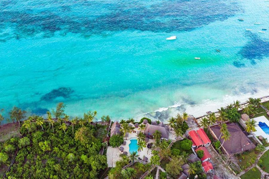 Aerial view of a beachfront resort with a pool, thatched roofs and turquoise water in Zanzibar