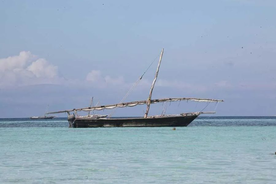 Traditional wooden dhow boat anchored in shallow turquoise water off Zanzibar's coast