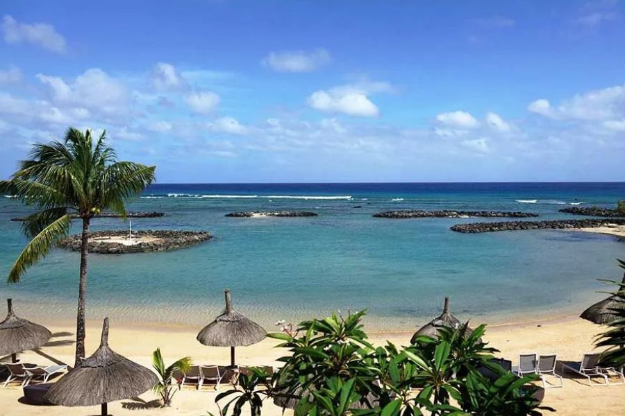 Resort beach with thatched umbrellas and loungers overlooking a calm turquoise bay