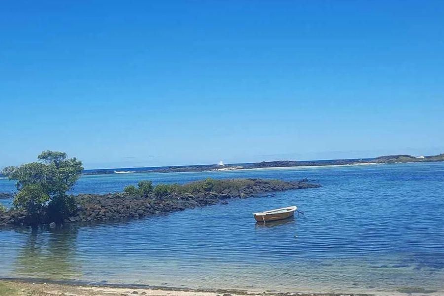 Small boat anchored in a calm bay near a rocky breakwater in Mauritius