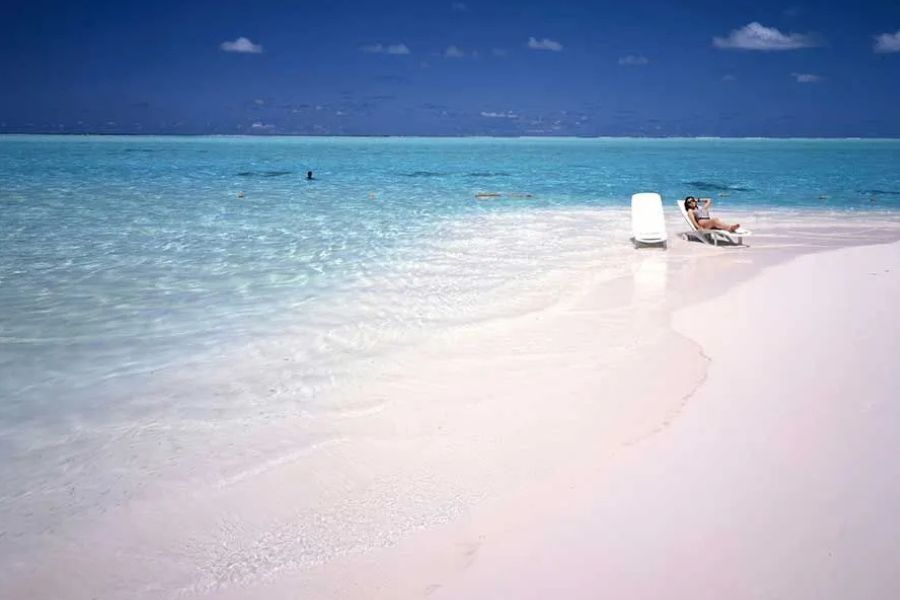 Woman relaxing on a lounger at the water's edge of a white sand beach in the Maldives