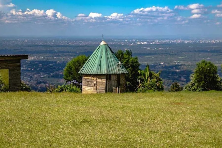 Traditional hut on a grassy hilltop overlooking a distant city in Kenya