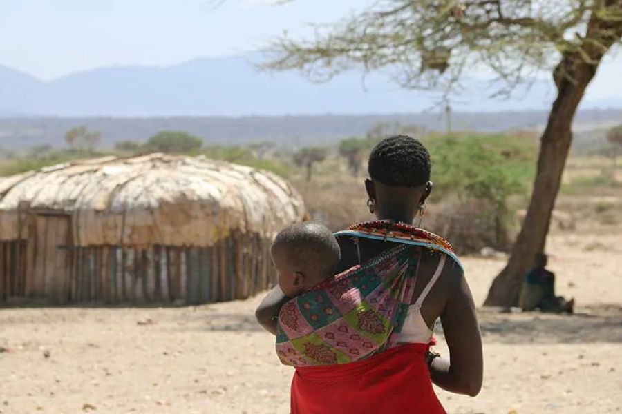 Samburu woman carrying a child near a traditional hut in rural Kenya