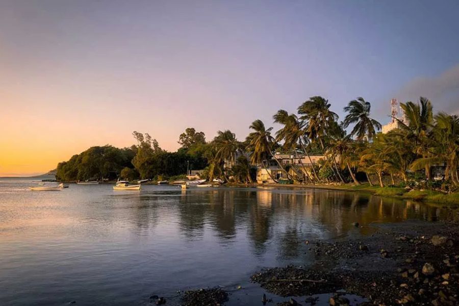 Small boats anchored in a calm bay at sunset, palm trees lining the shore