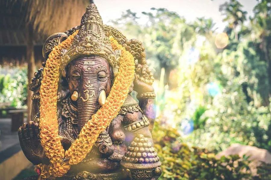 Stone Ganesha statue draped with a marigold garland in a tropical garden