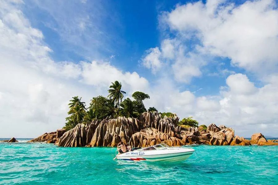 Small boat approaching a granite boulder islet in the Seychelles, turquoise water
