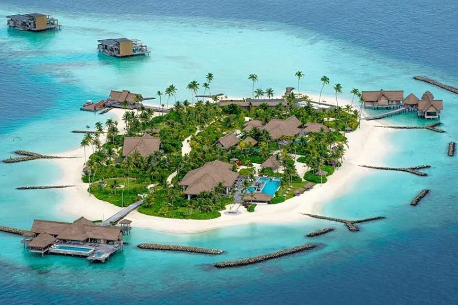 Aerial view of a small Maldives resort island with overwater bungalows and private pools