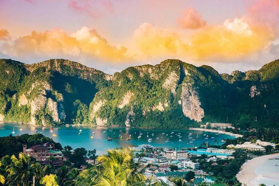 Phi Phi Islands bay with limestone cliffs, boats and beachfront buildings at sunset
