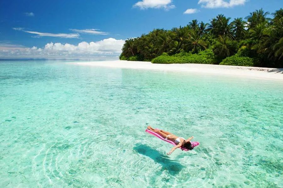 Woman relaxing in crystal-clear water beside a white-sand beach in the Maldives