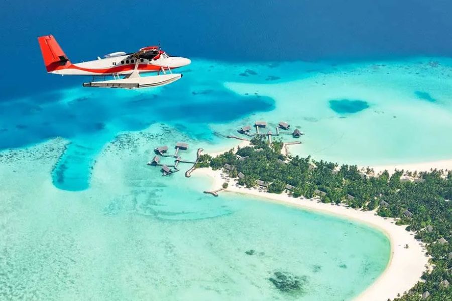 Seaplane flying above a luxury Maldives island resort and turquoise lagoon.