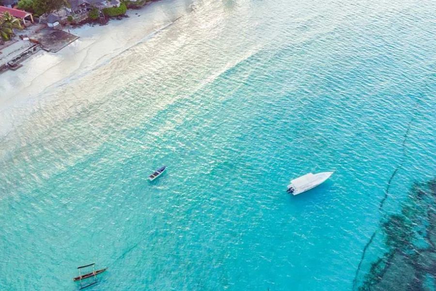 Aerial view of Zanzibar’s turquoise coast with boats near a white-sand beach.