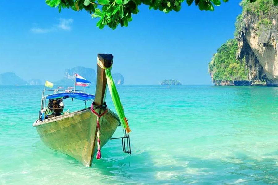 Traditional long-tail boat in turquoise waters near Thailand’s limestone islands.