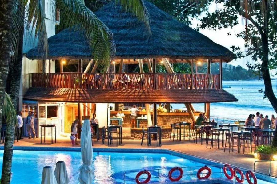 Poolside bar at a beachfront Seychelles resort surrounded by palm trees.