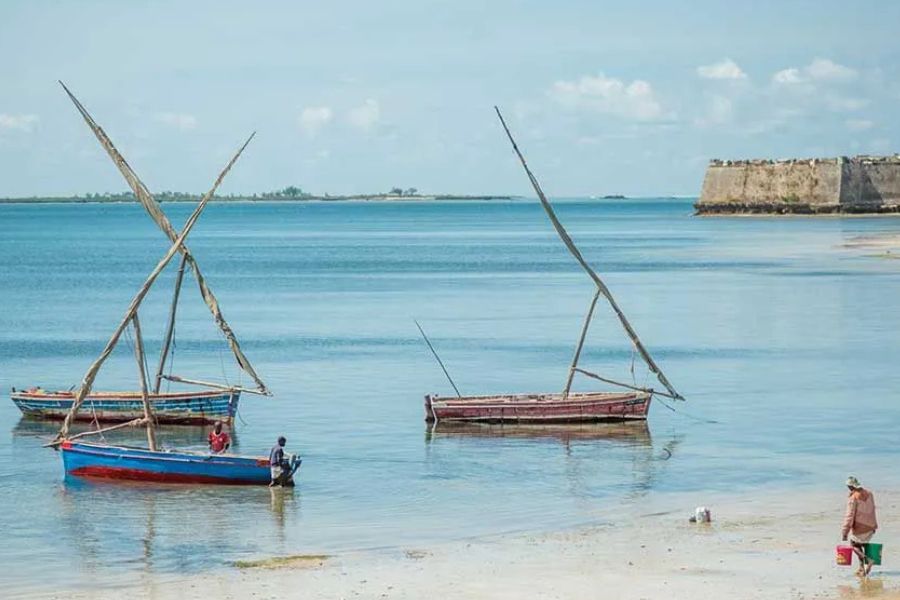 Traditional dhow boats beside a historic coastal fort in Mozambique.