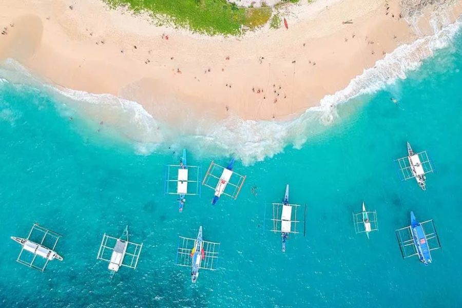 Aerial view of turquoise water and boats beside a tropical beach.