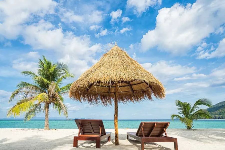 Sun loungers beneath a thatched umbrella on a peaceful tropical beach.