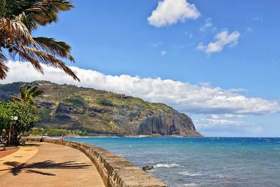Scenic coastal promenade beneath volcanic cliffs on Réunion Island.