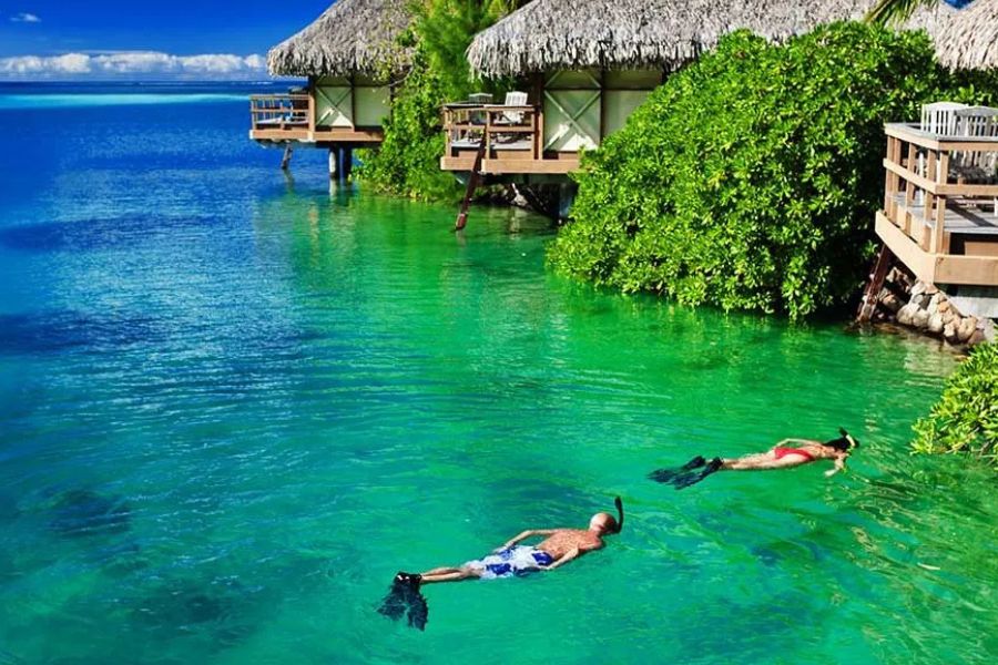 Couple snorkelling beside overwater bungalows in a crystal-clear Maldives lagoon.