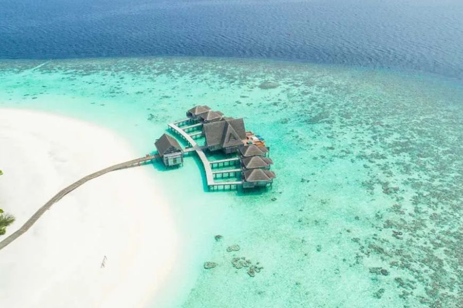 Aerial view of luxury overwater villas and a white-sand beach in the Maldives.