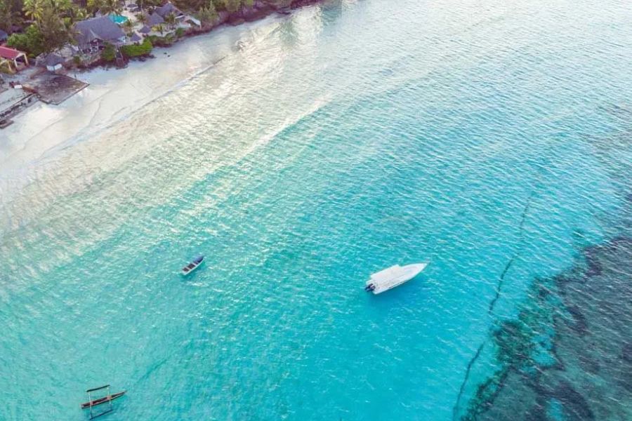 Aerial view of boats floating in turquoise water along a tropical white sand beach