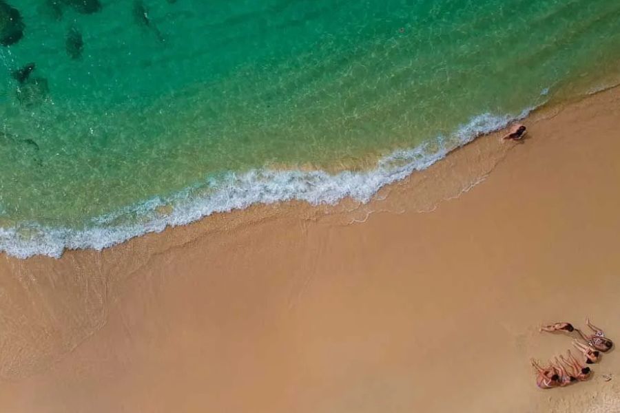 Aerial view of people sunbathing on a sandy beach with turquoise ocean waves