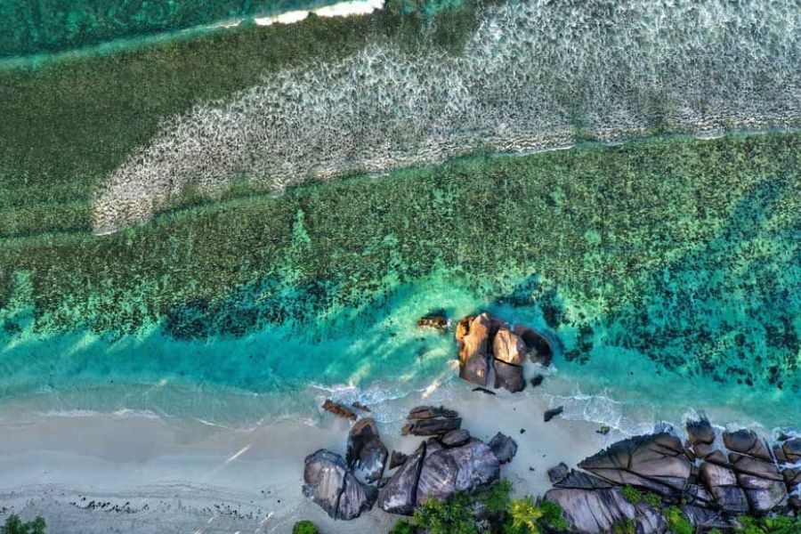 Aerial view of granite rocks on a sandy beach with clear coral reef waters