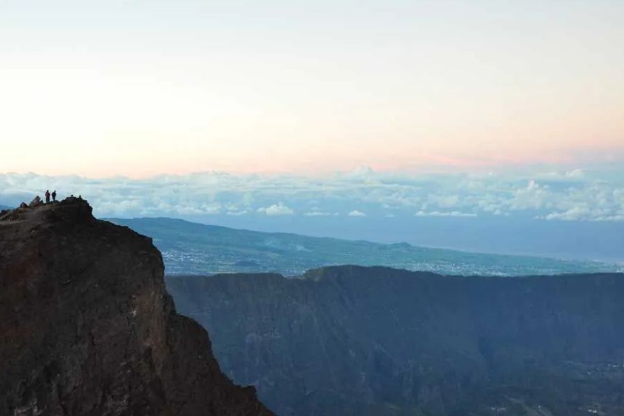 Hikers standing on a cliff edge overlooking a vast volcanic caldera and ocean view
