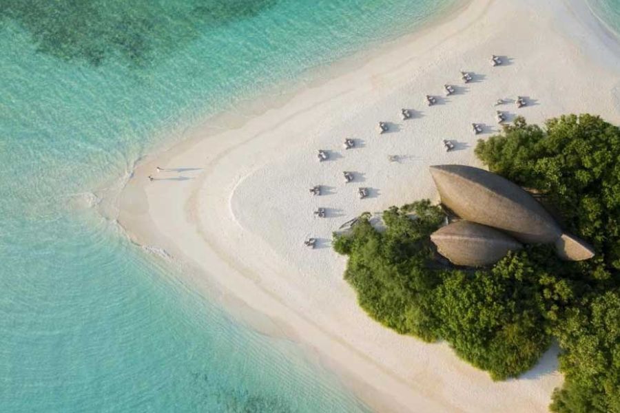 Aerial view of a white sand beach resort with unique leaf-shaped thatched roofs