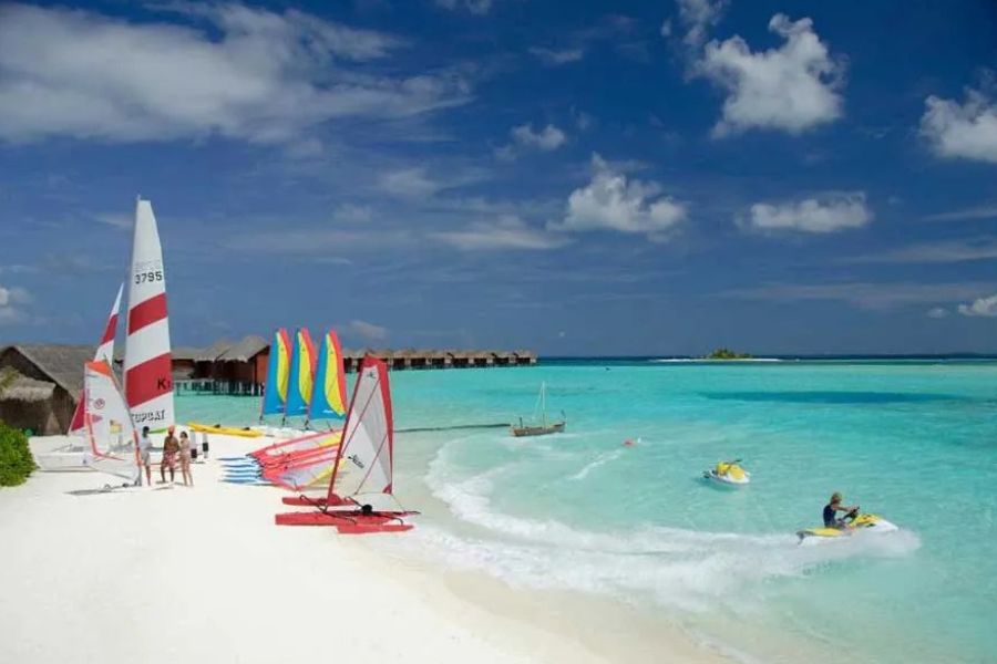 Tropical beach with sailboats, jet skis, and water sports equipment in turquoise sea