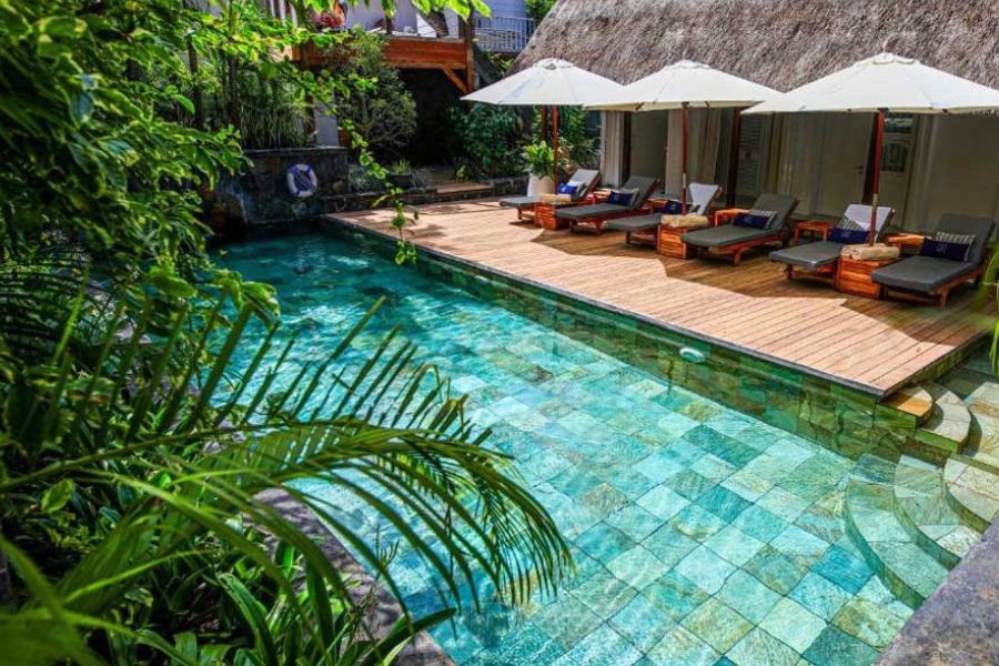 Private resort swimming pool with wooden deck, sun loungers, and tropical plants