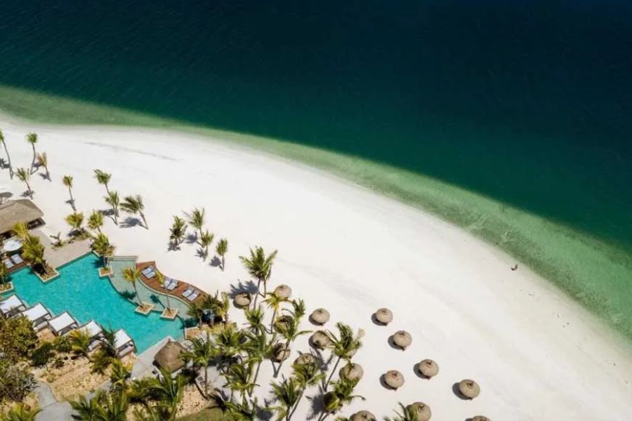 Aerial view of a white sand beach resort with palm trees and turquoise ocean water