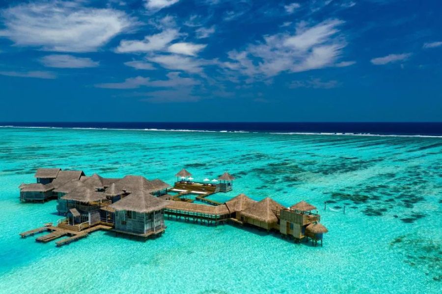 Aerial view of overwater luxury villas connected by wooden boardwalks in a turquoise lagoon