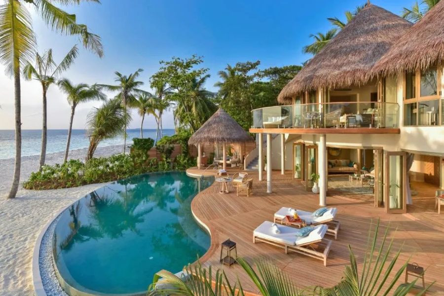 Luxury beachfront villa with a private pool, wooden deck, and thatched roof next to palm trees